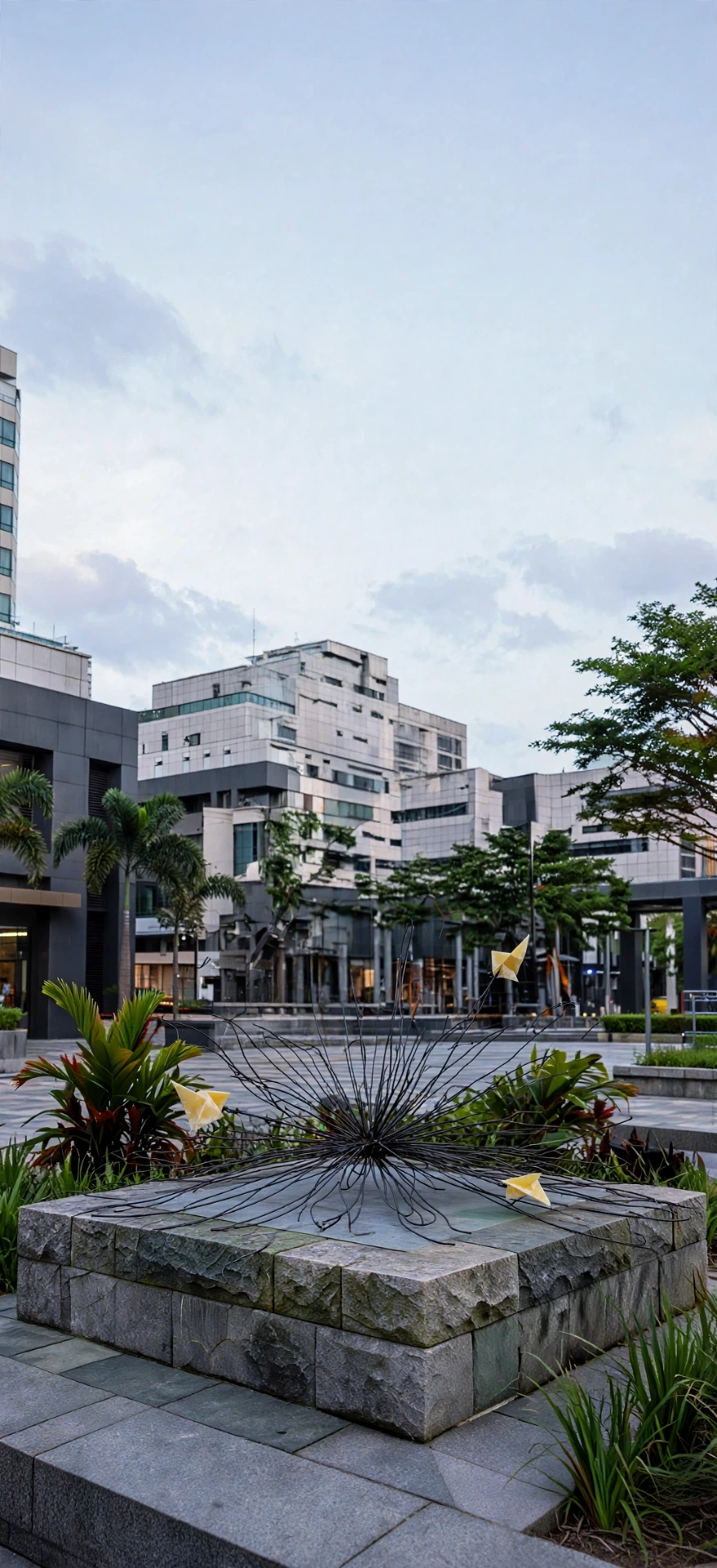 Senbazuru — a low steel filament burst with yellow onyx folds in a plaza garden.