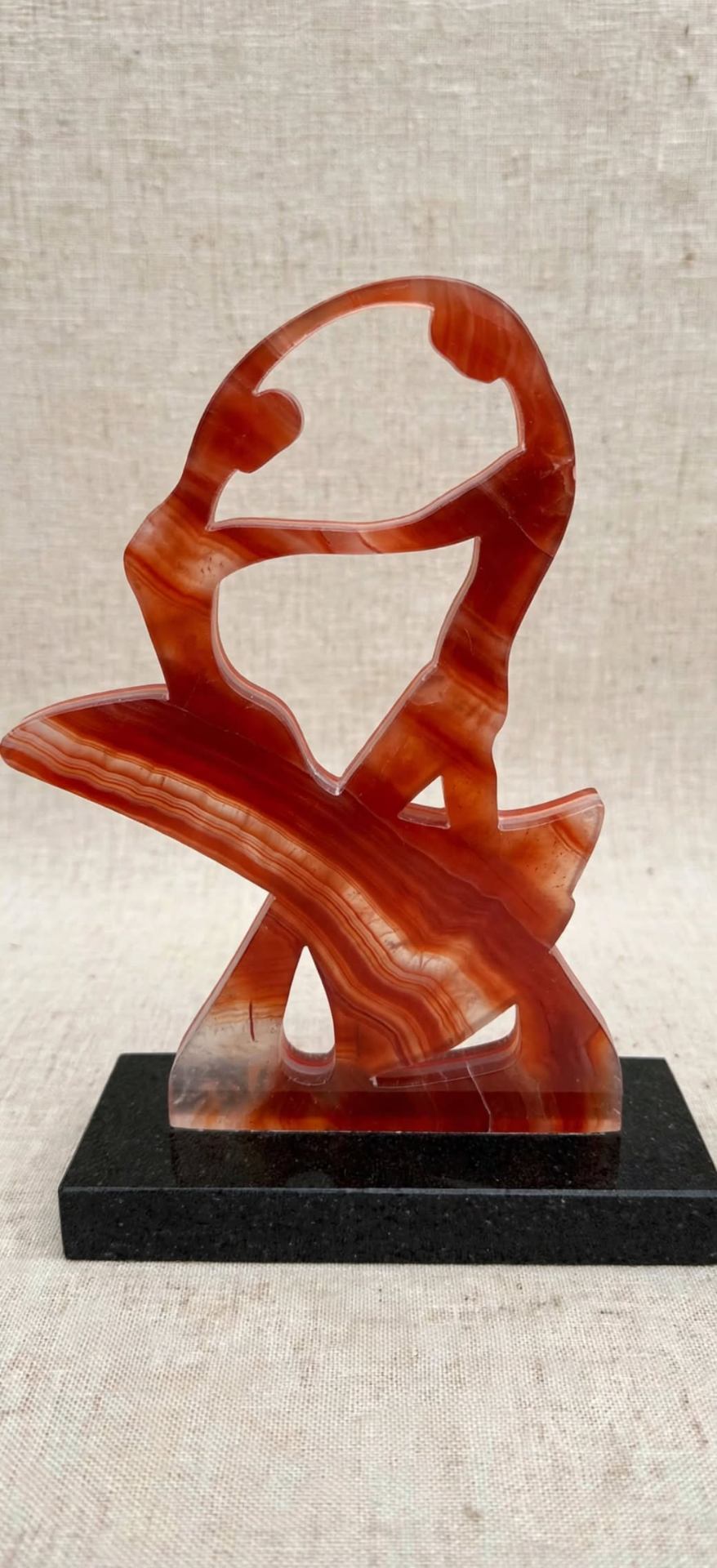 Tango Cut — a translucent banded red agate sculpture of a dancing pair, on a black granite base.