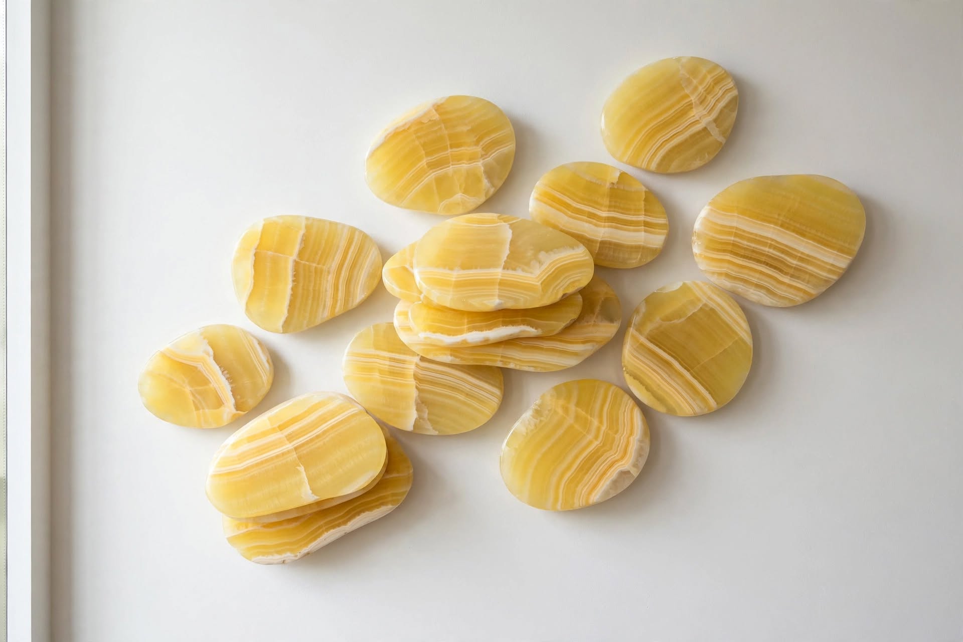 Rainfall — a cluster of polished yellow onyx droplet forms arranged across a white wall.