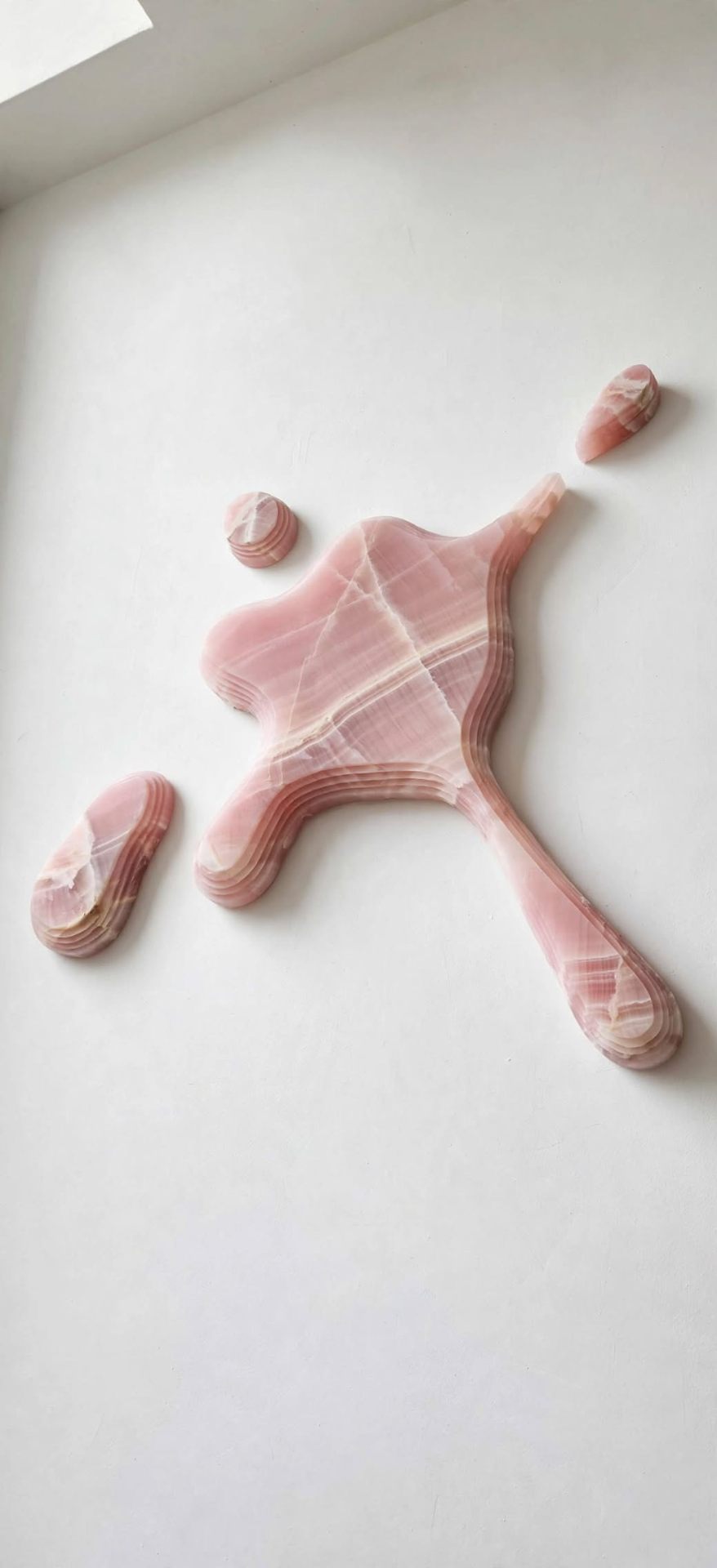 Still Water — a pink onyx splash form with satellite droplets mounted on a white wall.